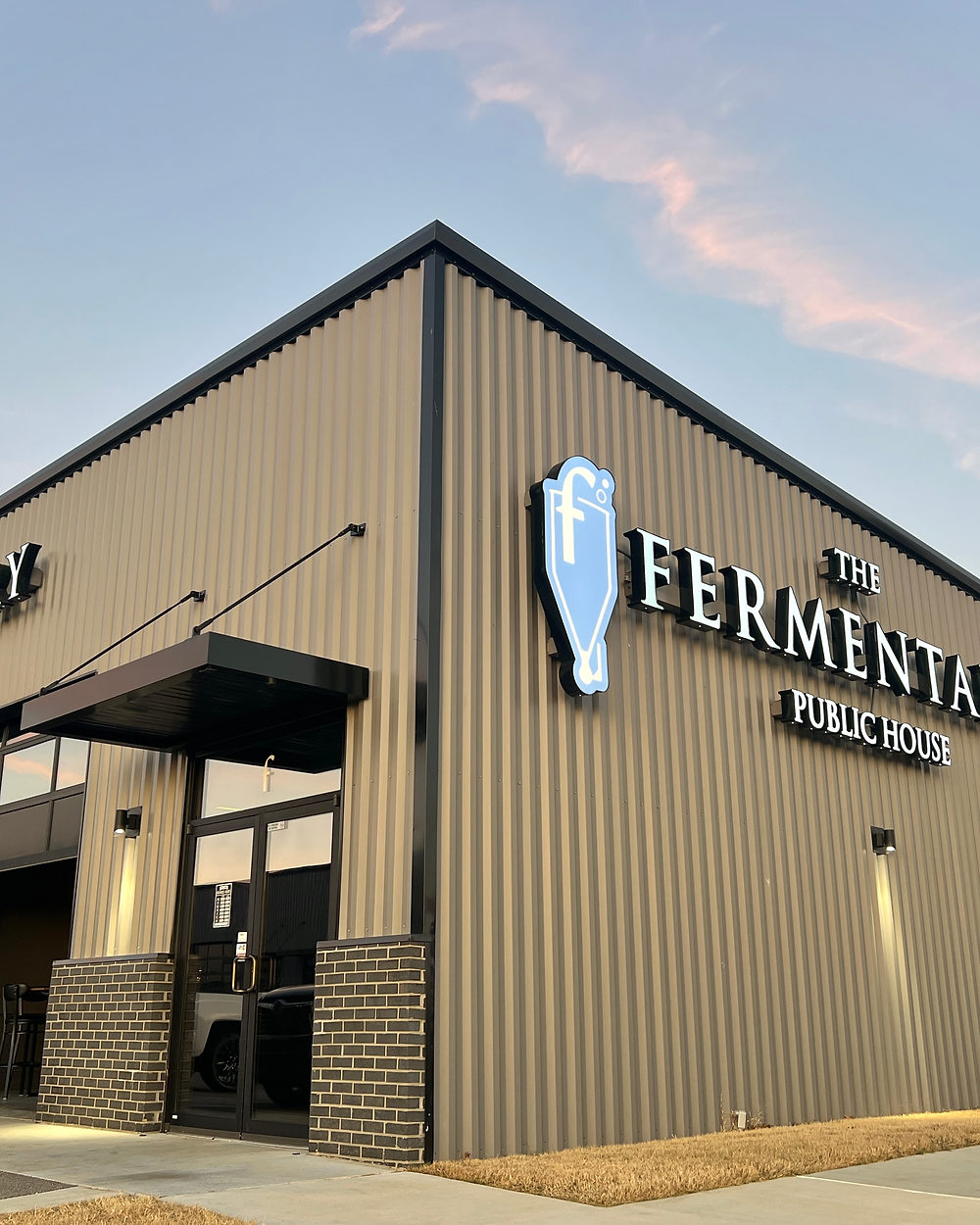 The Fermentary Public House at dusk, the illuminated fermenter sign on the corner of the building.