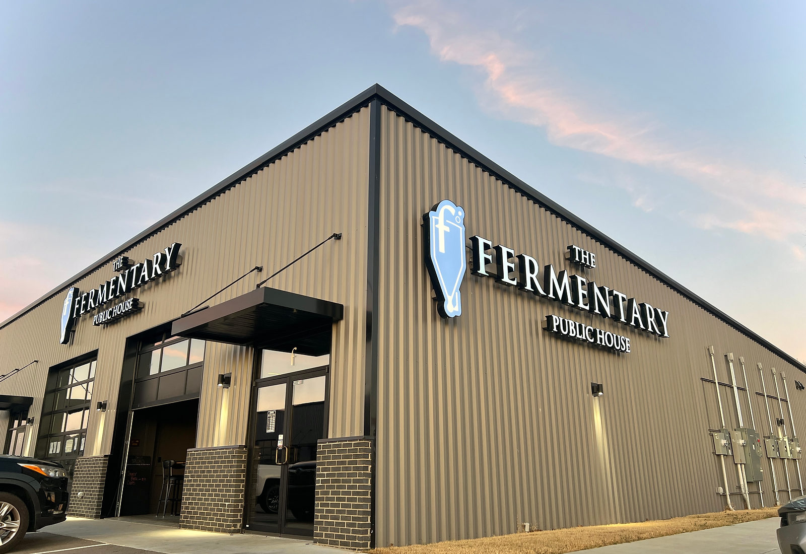 The Fermentary Public House at dusk, the illuminated fermenter logo on the corner of the building.