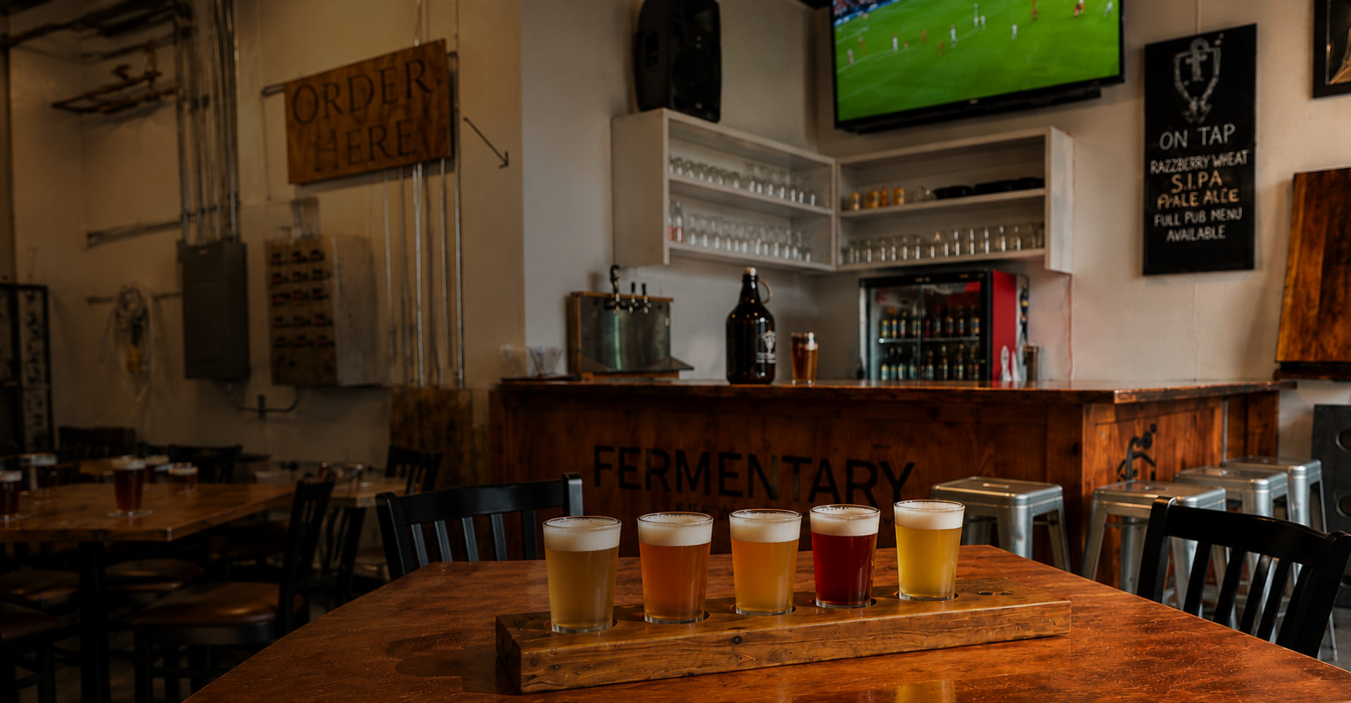 A flight of five house beers on a wooden paddle in the Fermentary brewery, its name carved into the bar behind.