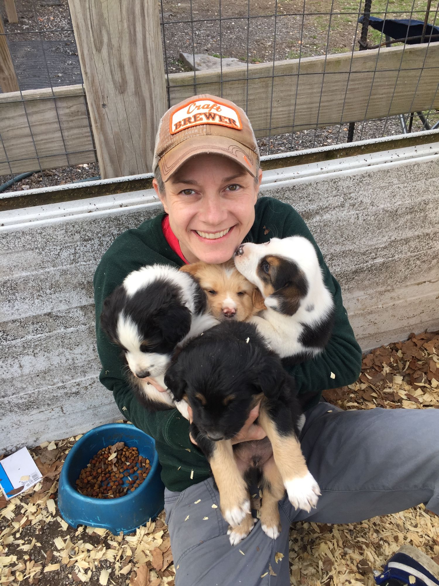 Co-owner Jennifer Muckerman in a Craft Brewer cap, smiling and holding an armful of puppies.